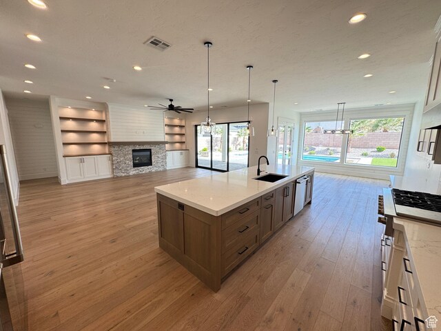 kitchen with a sink, a stone fireplace, light wood finished floors, dishwasher, and a ceiling fan
