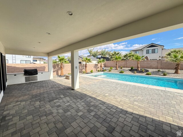 view of swimming pool featuring a patio, an outdoor kitchen, a fenced backyard, and a pool with connected hot tub