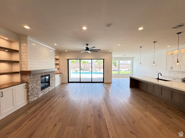 unfurnished living room featuring a sink, a stone fireplace, light wood-style flooring, ceiling fan, and recessed lighting