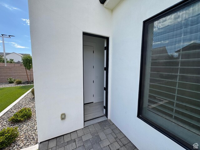 view of exterior entry featuring stucco siding and fence