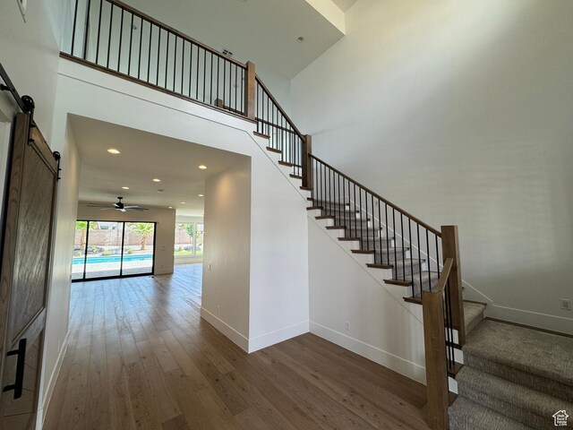 staircase featuring a barn door, hardwood / wood-style floors, baseboards, ceiling fan, and recessed lighting