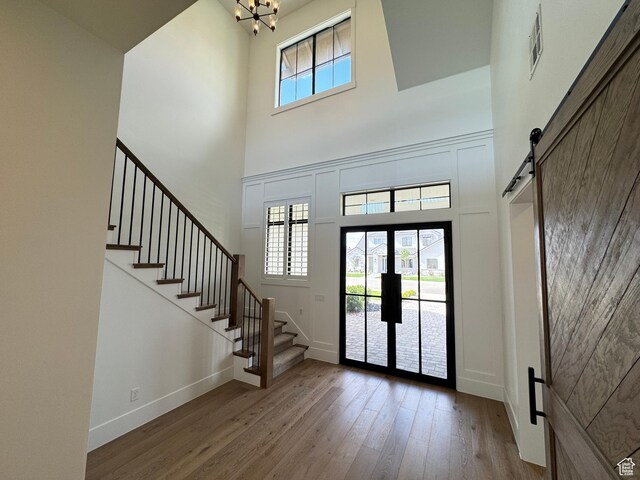 foyer with a high ceiling, a barn door, stairway, wood-type flooring, and a chandelier
