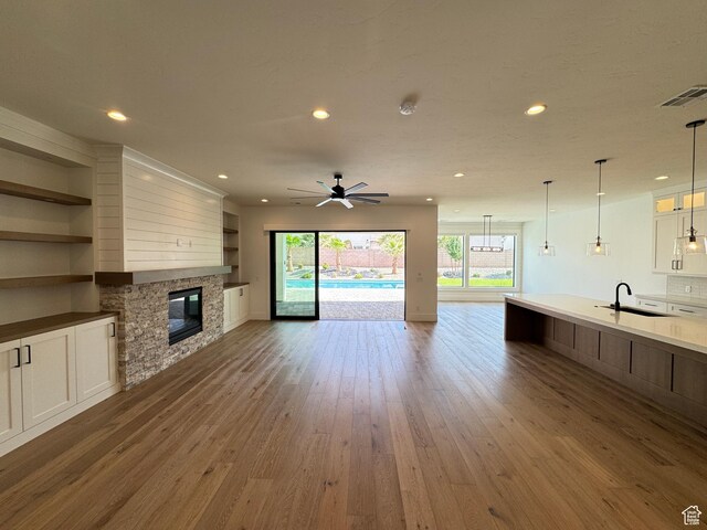 unfurnished living room with a sink, wood finished floors, a fireplace, ceiling fan, and recessed lighting
