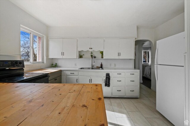 kitchen featuring freestanding refrigerator, electric range, a sink, arched walkways, and white cabinetry