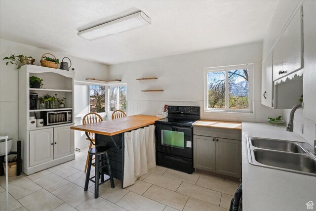 kitchen with black electric range oven, open shelves, a sink, a breakfast bar area, and light tile patterned floors