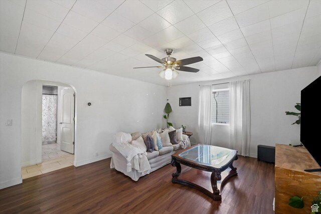 living room featuring arched walkways, ceiling fan, wood finished floors, and baseboards