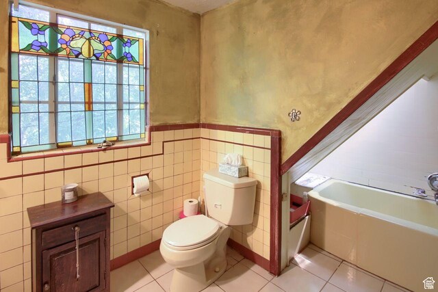 bathroom with toilet, tile patterned flooring, a tub, tile walls, and a wainscoted wall