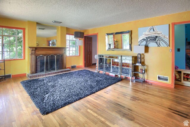 living room with a textured ceiling, wood finished floors, a brick fireplace, and baseboards