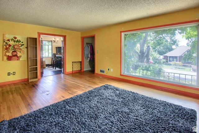 empty room with wood finished floors, a chandelier, a textured ceiling, and baseboards