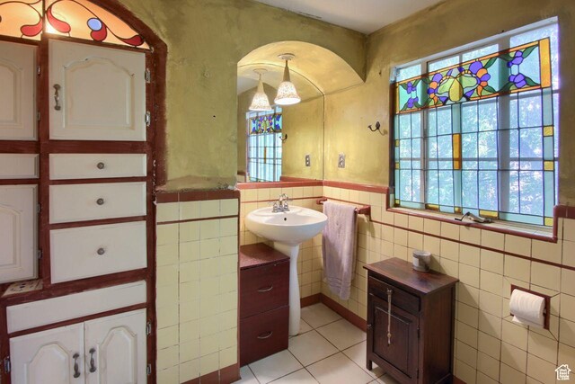 bathroom featuring tile patterned floors, tile walls, plenty of natural light, a wainscoted wall, and a sink