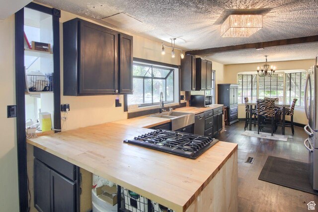 kitchen with butcher block countertops, a sink, stainless steel appliances, a textured ceiling, and dark wood-type flooring