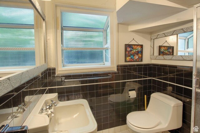 half bathroom with toilet, tile walls, a sink, and wainscoting