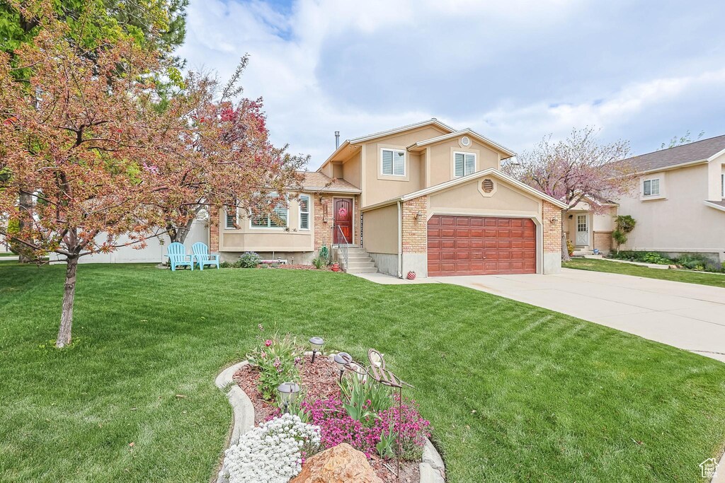 view of front of property with stucco siding, concrete driveway, a front lawn, a garage, and brick siding