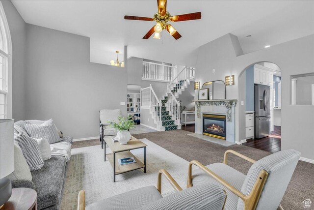 living room featuring ceiling fan, carpet, arched walkways, baseboards, and a high ceiling