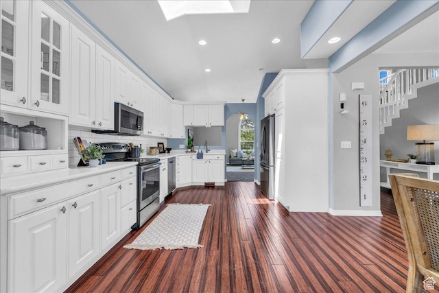 kitchen featuring appliances with stainless steel finishes, glass insert cabinets, light countertops, decorative backsplash, and white cabinets