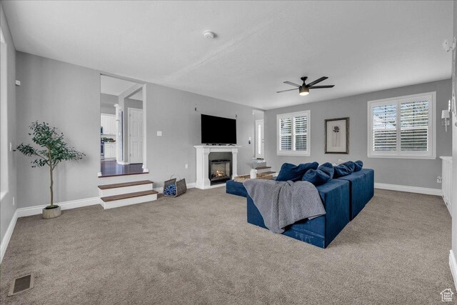 carpeted living room with a ceiling fan, baseboards, and a glass covered fireplace