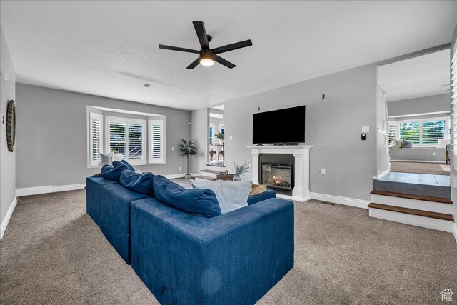 living room with carpet, a ceiling fan, baseboards, and a glass covered fireplace
