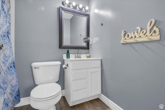 bathroom with baseboards, toilet, wood finished floors, and vanity