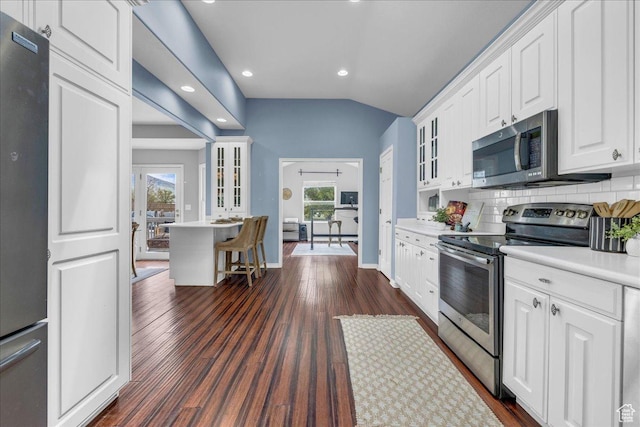 kitchen with appliances with stainless steel finishes, glass insert cabinets, white cabinetry, light countertops, and tasteful backsplash