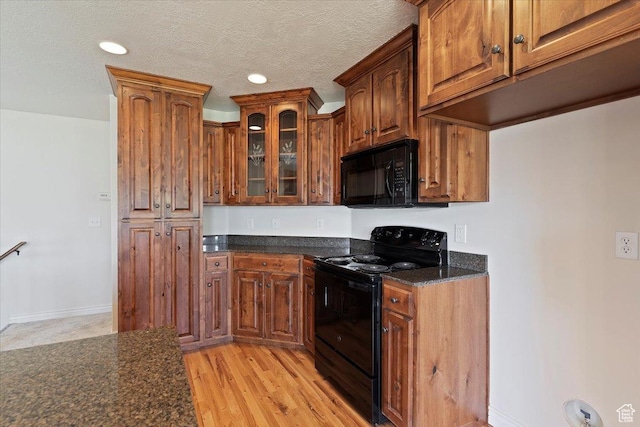 kitchen featuring black appliances, glass insert cabinets, brown cabinets, light wood-style floors, and a textured ceiling