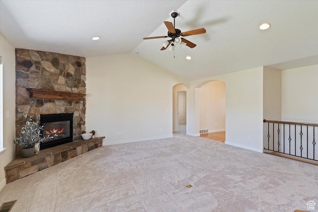 unfurnished living room with ceiling fan, arched walkways, carpet floors, vaulted ceiling, and a fireplace
