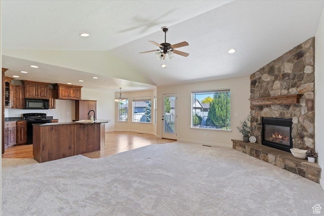 kitchen with black appliances, open floor plan, light carpet, vaulted ceiling, and a stone fireplace