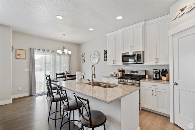 kitchen with stainless steel appliances, a sink, light wood-style floors, an island with sink, and white cabinets