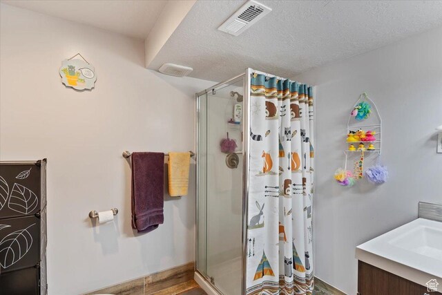 bathroom featuring a shower stall, a textured ceiling, wood finished floors, and vanity