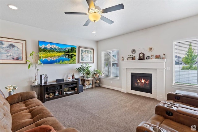 living area with a glass covered fireplace, ceiling fan, carpet, and baseboards