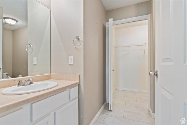 bathroom with tile patterned floors, vanity, toilet, a spacious closet, and baseboards