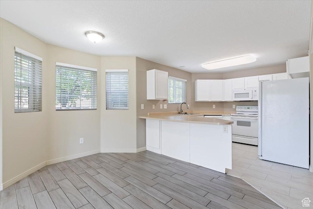 kitchen with white appliances, a sink, a peninsula, light countertops, and white cabinetry