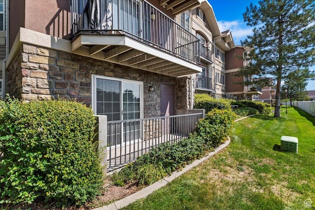 view of side of property featuring stone siding, a balcony, a yard, and stucco siding