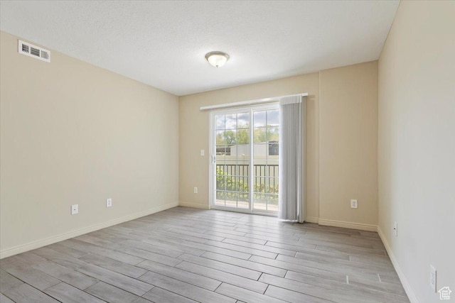 unfurnished room featuring light wood-style floors, baseboards, and a textured ceiling