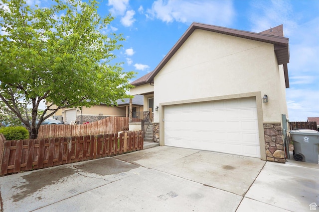 view of side of property featuring stone siding, stucco siding, concrete driveway, fence, and an attached garage