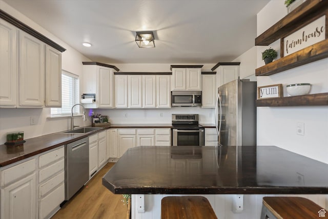 kitchen featuring appliances with stainless steel finishes, a sink, open shelves, dark countertops, and a kitchen breakfast bar