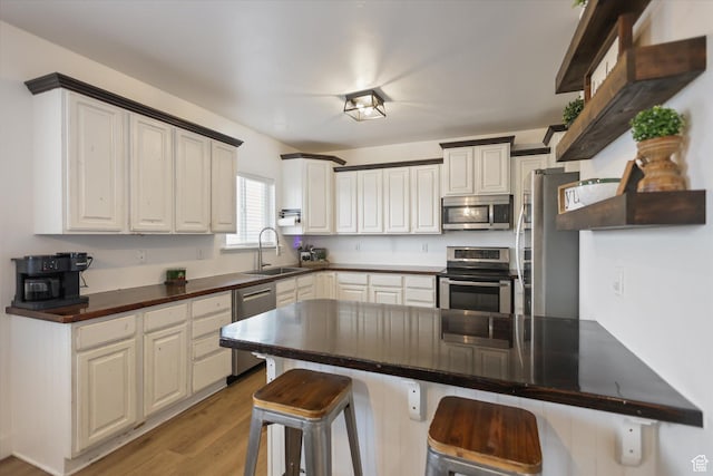 kitchen featuring stainless steel appliances, a sink, a breakfast bar area, light wood-style floors, and a peninsula