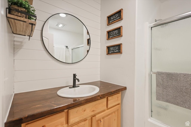 bathroom featuring a shower with door, vanity, and wooden walls