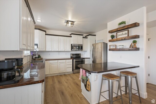 kitchen featuring stainless steel appliances, open shelves, a sink, a kitchen breakfast bar, and dark countertops