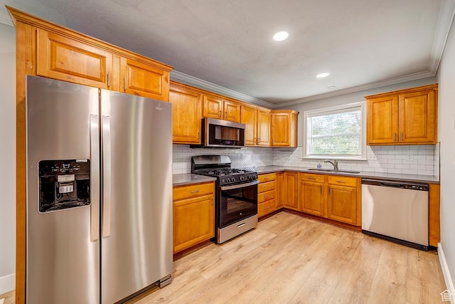 kitchen with appliances with stainless steel finishes, a sink, crown molding, light wood-style flooring, and brown cabinets