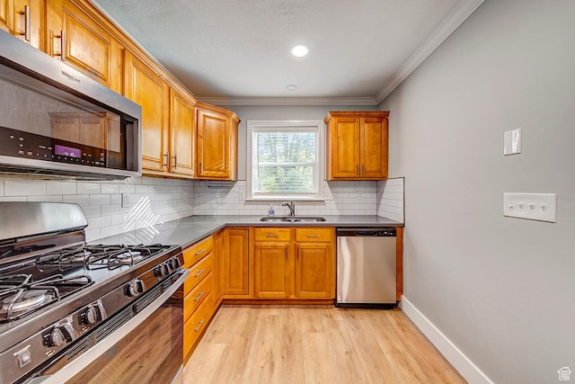 kitchen with appliances with stainless steel finishes, a sink, light wood-style flooring, brown cabinets, and crown molding