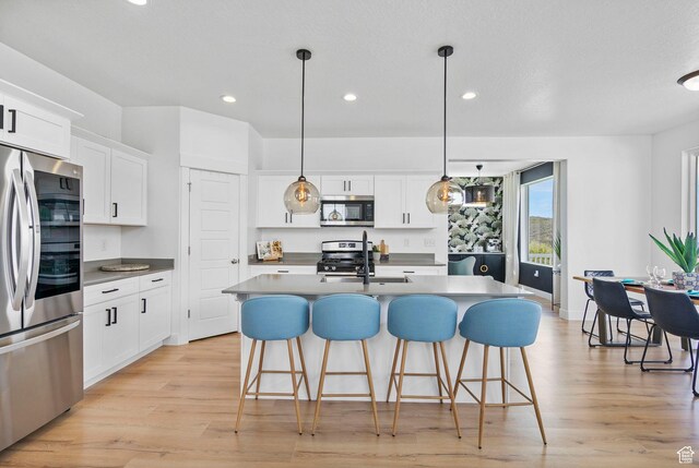 kitchen featuring appliances with stainless steel finishes, light wood-style flooring, recessed lighting, white cabinetry, and a kitchen bar