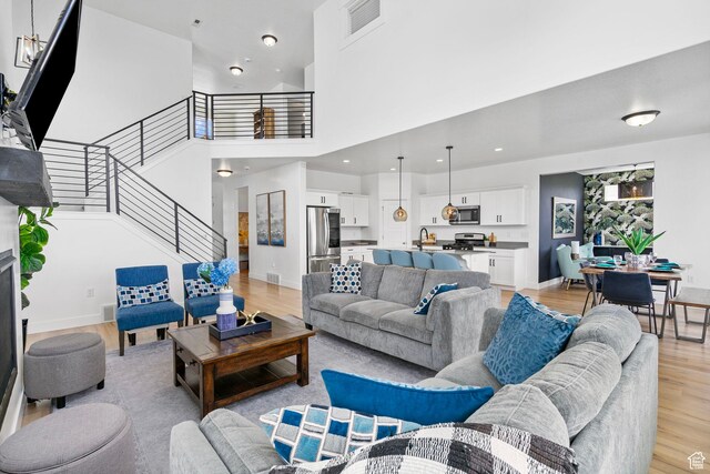 living area featuring light wood-style flooring, stairs, a high ceiling, and baseboards