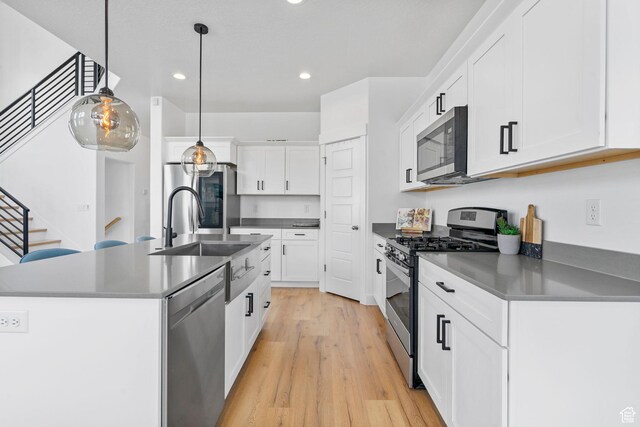 kitchen with stainless steel appliances, dark countertops, recessed lighting, light wood-style floors, and a sink
