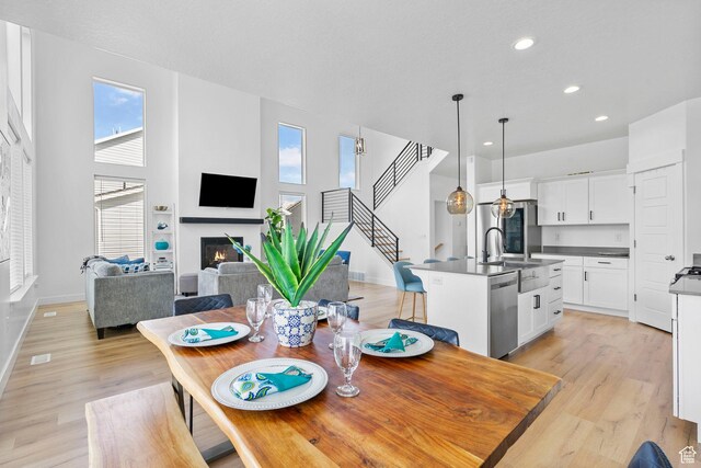 dining room featuring recessed lighting, light wood finished floors, baseboards, a glass covered fireplace, and stairs
