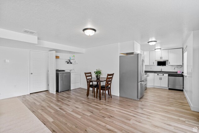 kitchen featuring stainless steel appliances, light wood-style floors, white cabinetry, dark countertops, and a sink