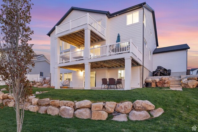 back of property at dusk with a balcony, a patio area, and a yard