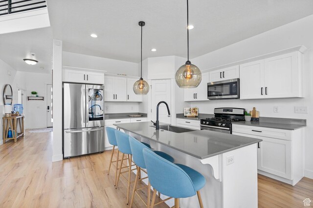 kitchen with appliances with stainless steel finishes, a sink, dark countertops, light wood-type flooring, and recessed lighting