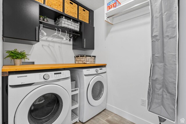 clothes washing area with washing machine and dryer, cabinet space, light wood-style flooring, and baseboards