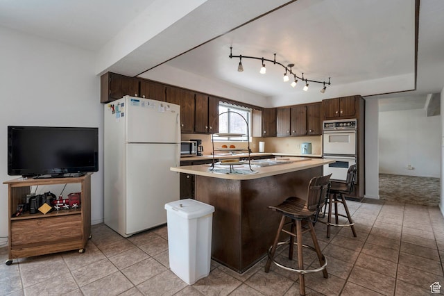 825 W Arapahoe Ave S, Salt Lake City, UT 84104 - kitchen featuring white appliances, dark brown cabinetry, light countertops, and a kitchen breakfast bar