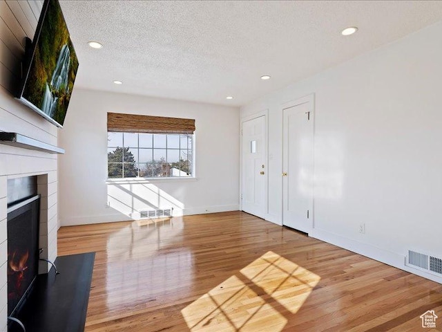 unfurnished living room featuring wood finished floors, a warm lit fireplace, a textured ceiling, baseboards, and recessed lighting